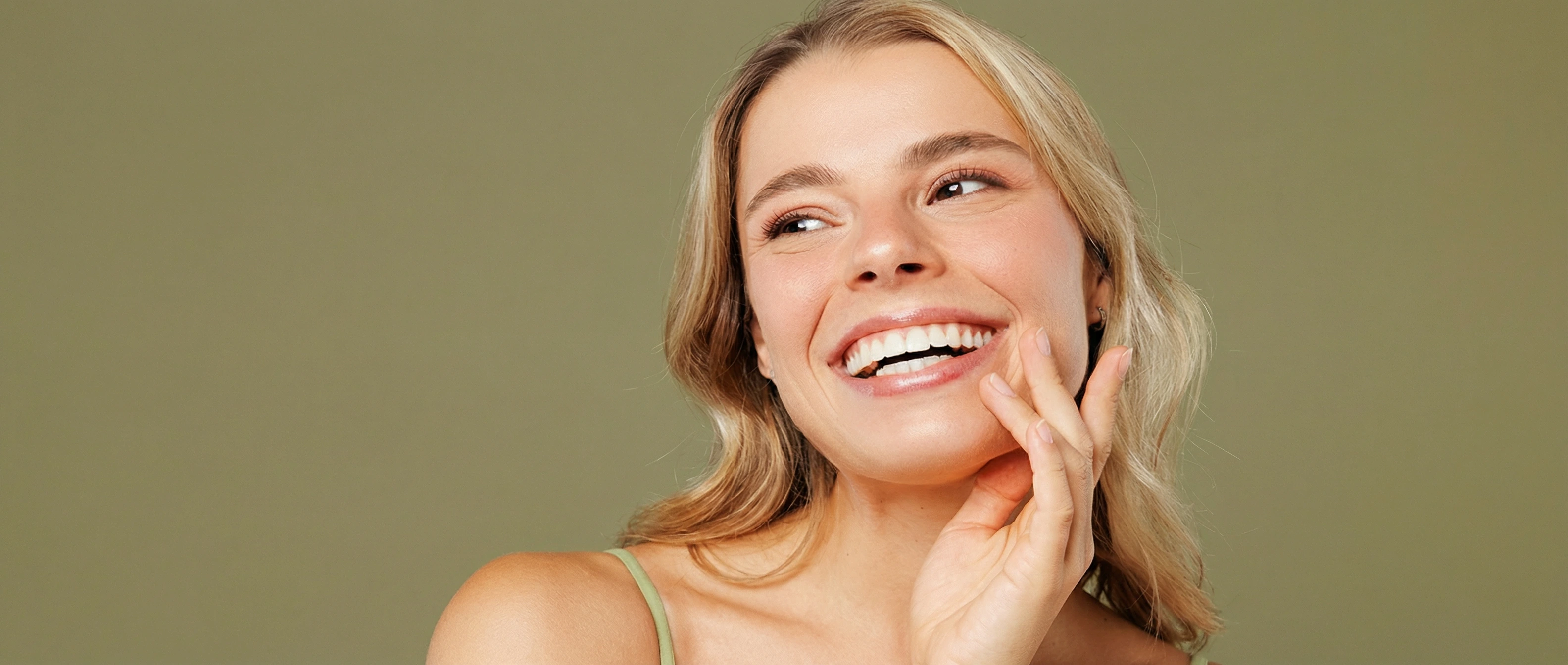 Young woman with smooth, radiant skin smiling and touching her chin after Alma Opus Plasma treatment